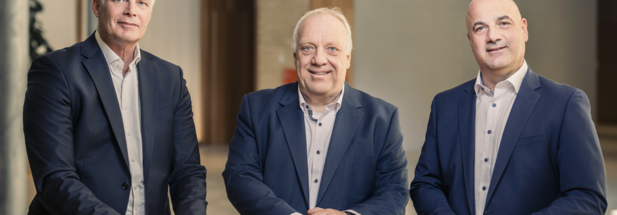 Drei Männer in blauen Anzügen stehend vor einem Tisch. Von links nach rechts: Ralph Wildermuth, Geschäftsführer der W&W Informatik, Johannes Rohé, Mitgleid der Geschäftsleitung HOLISTIC42 GmbH und Thomas Reitz, Geschäftsführer der HOLISTIC42 GmbH